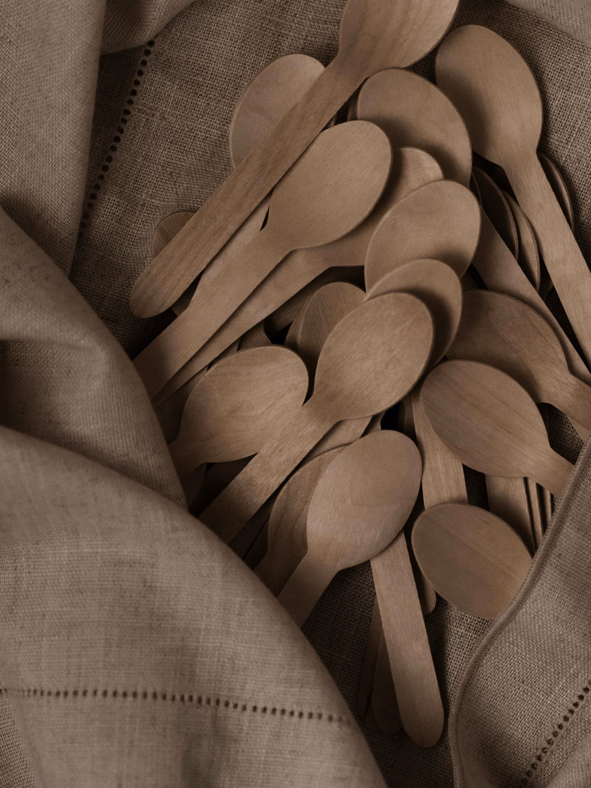 Petites cuillères en bois clair rassemblées dans un linge de lin taupe à jours