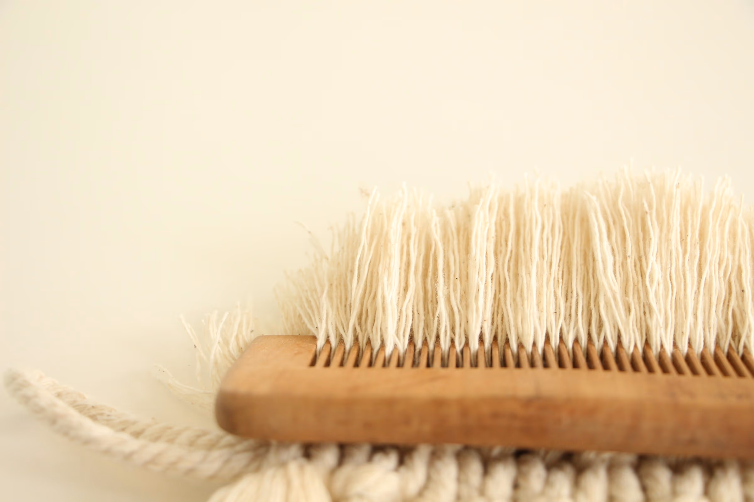 Brosse en bois aux fibres naturelles écrues posée sur une étoffe frangée, fond crème