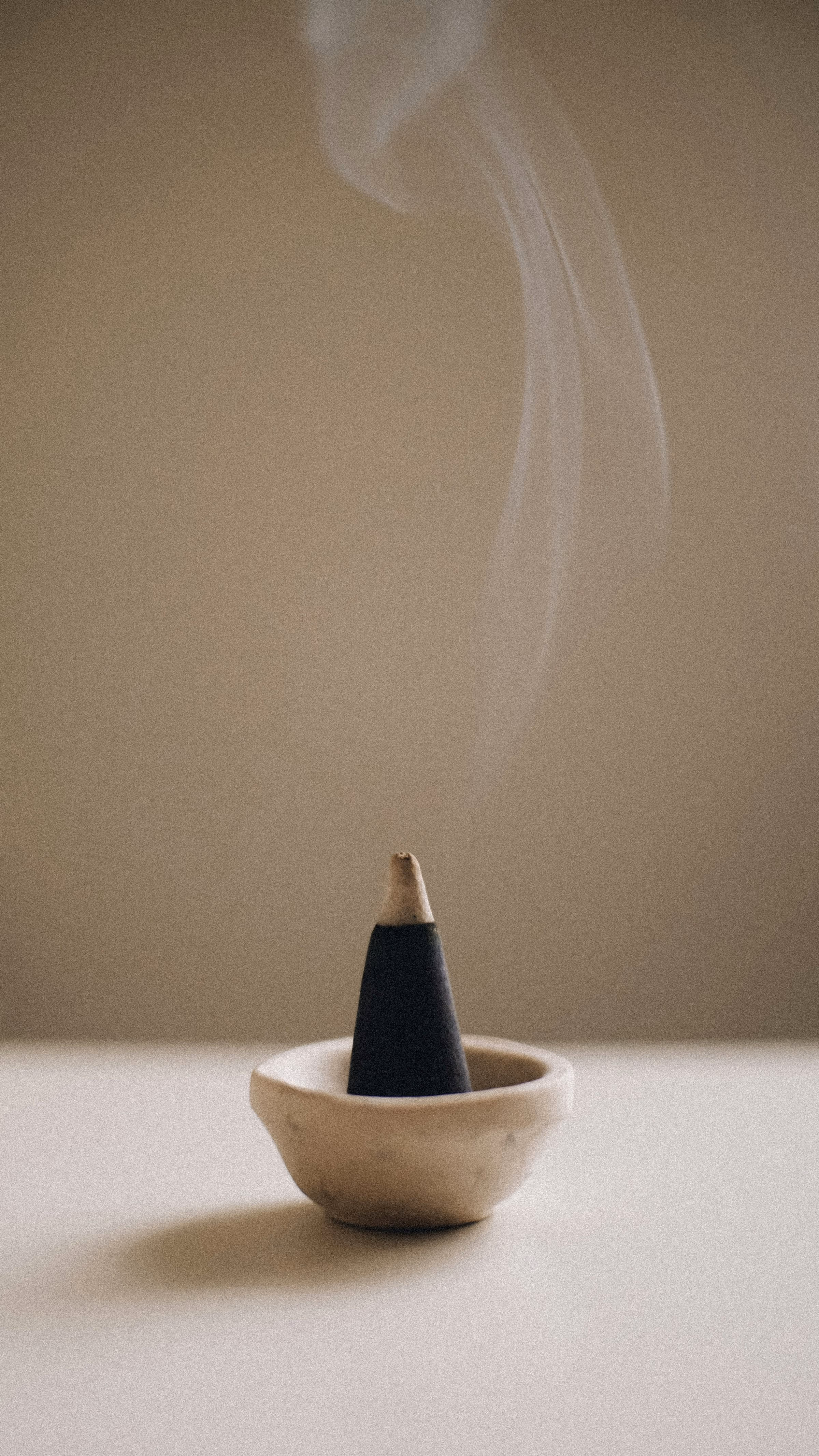Cône d’encens fumant dans une petite coupelle en céramique, sur fond beige