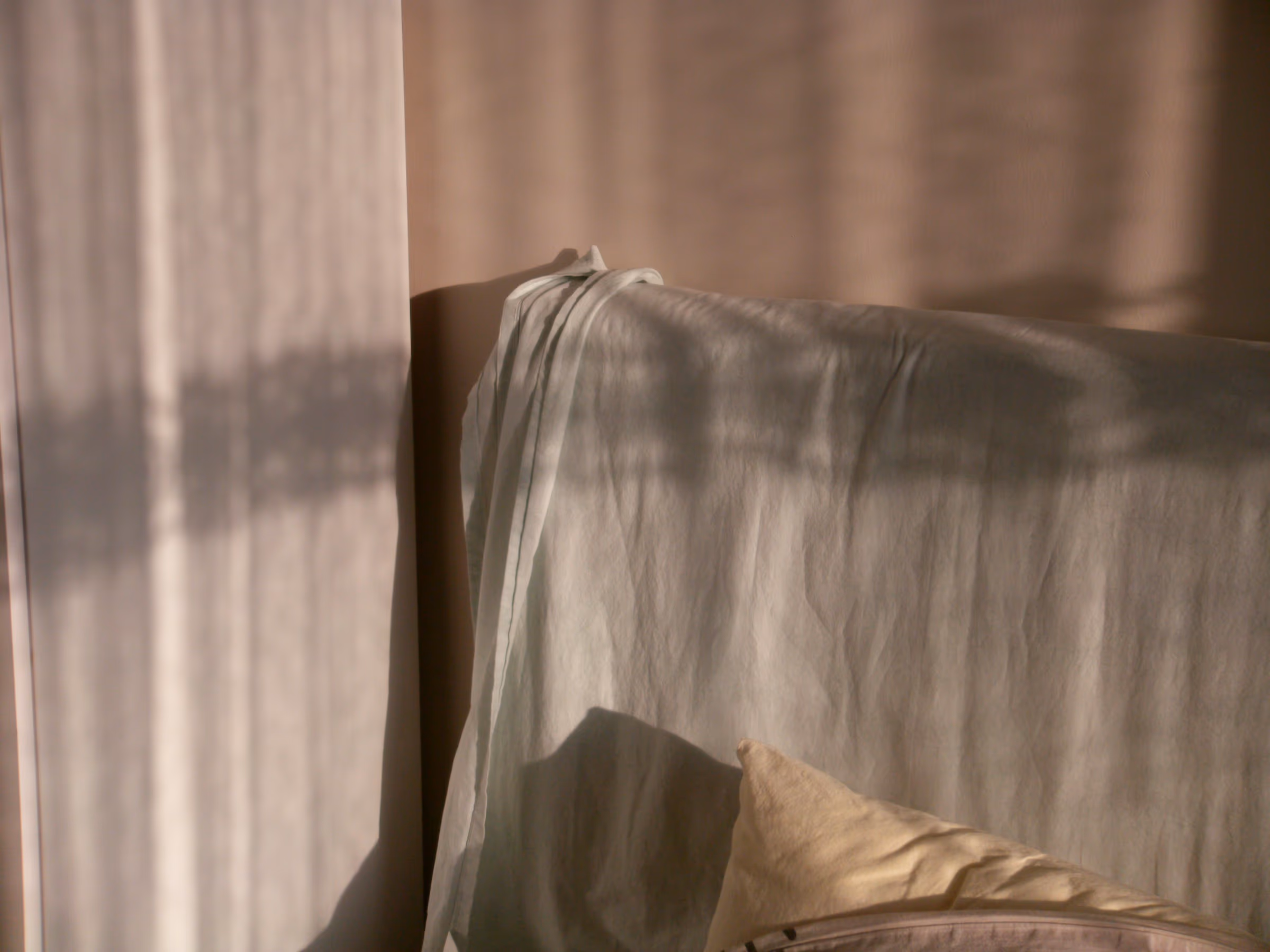 Canapé recouvert d’un drap clair, strié d’ombres et de lumière du soleil filtrées par un voilage