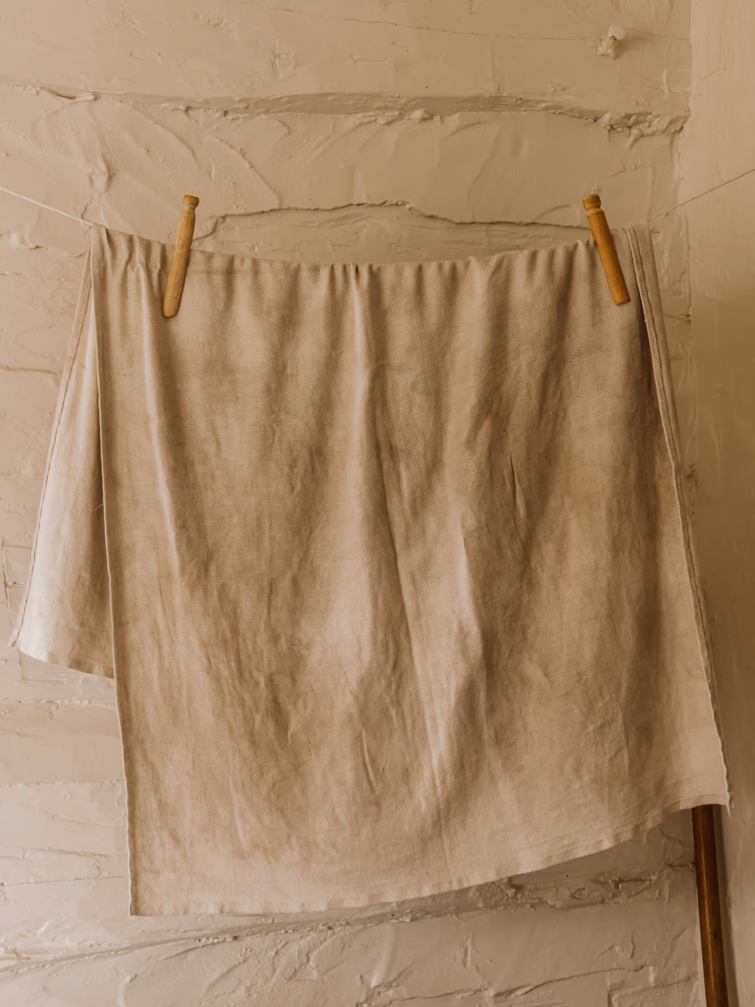 Linge en lin naturel suspendu par deux pinces en bois contre un mur blanc chaulé