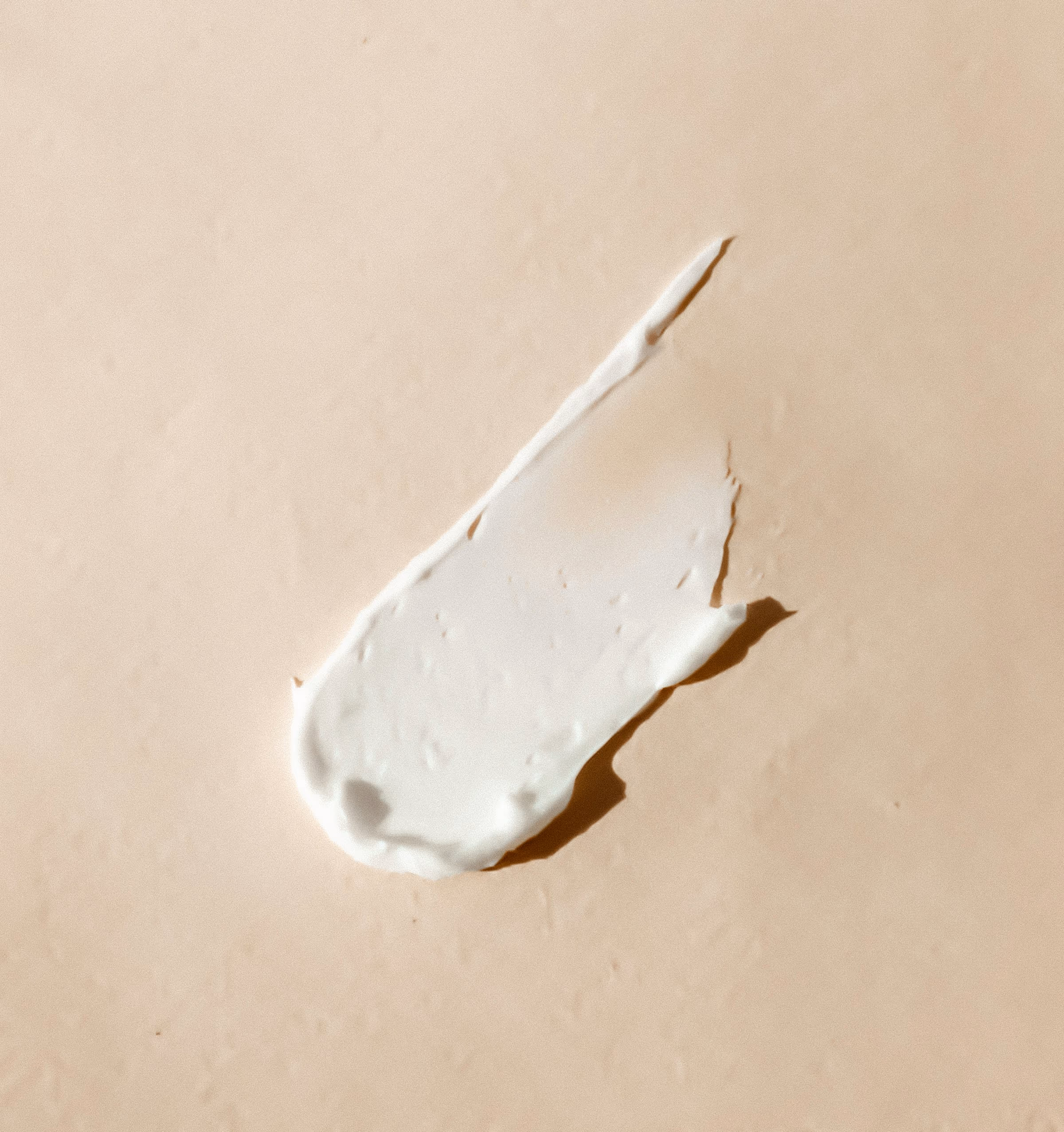 Trace de crème blanche étalée sur un fond beige, avec une ombre portée nette