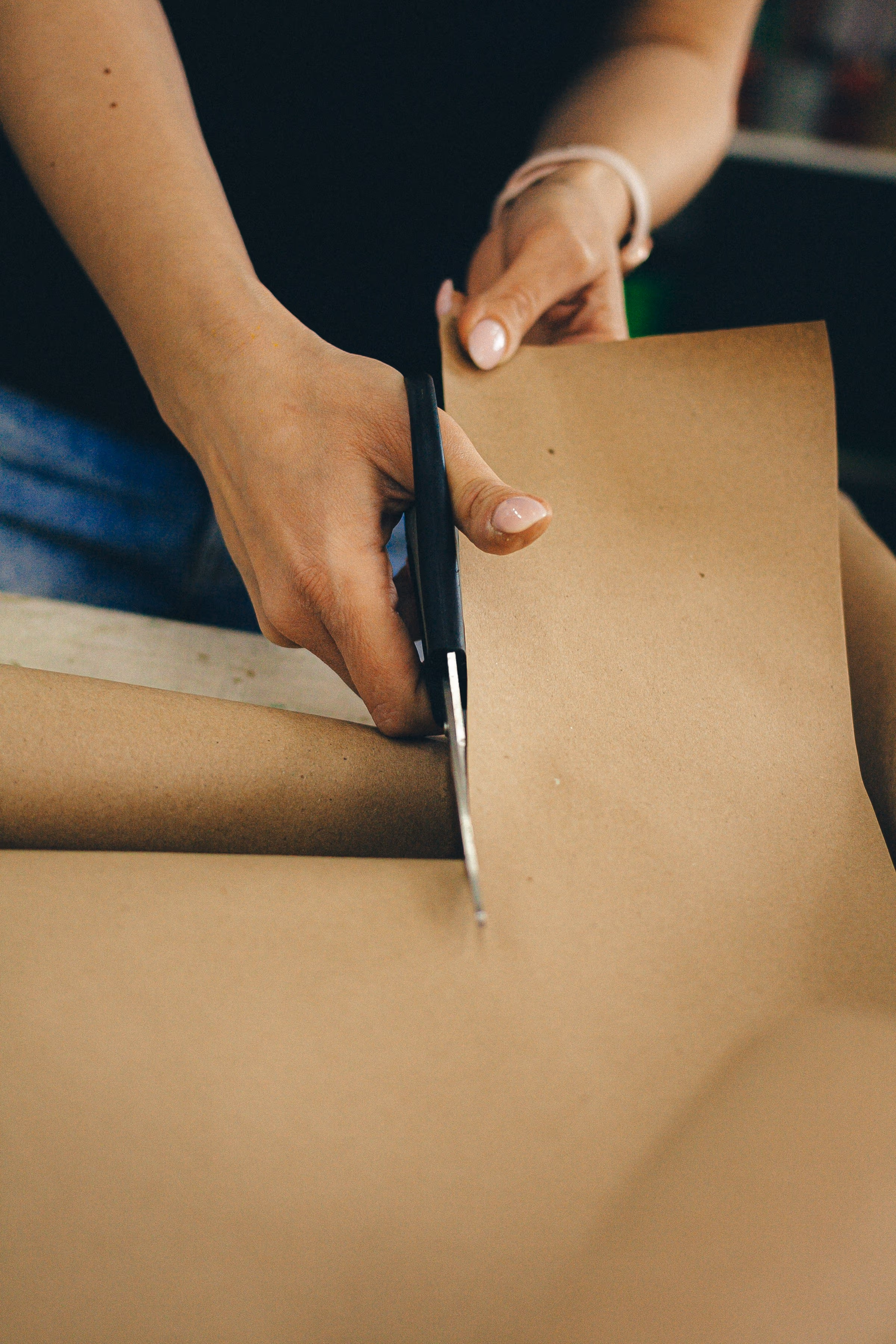 Mains découpant une feuille de papier kraft sur un plan de travail