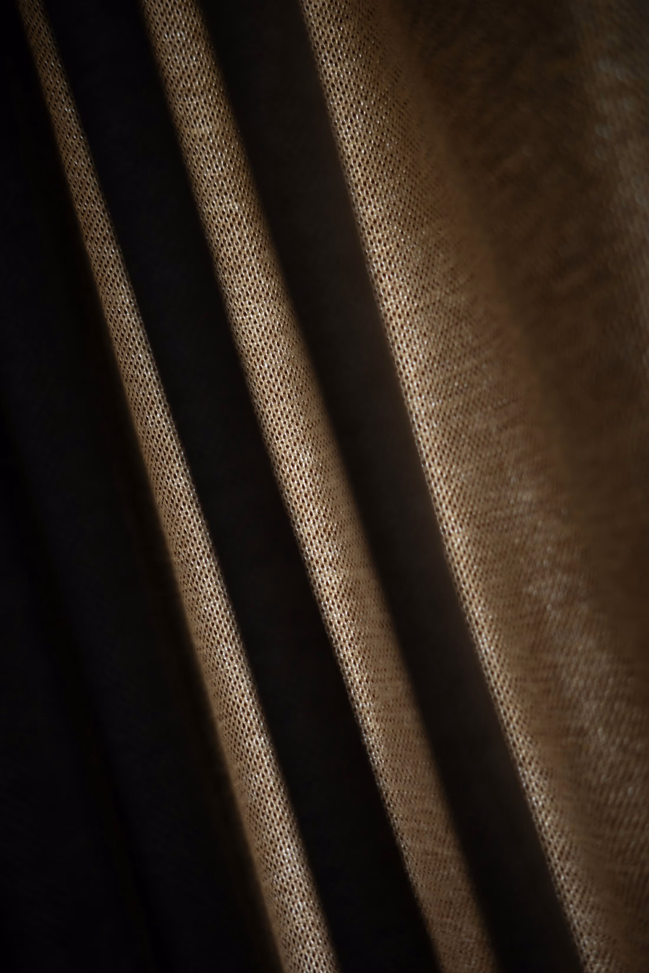 Plis d’un rideau épais au tissage serré, couleur bronze, dans une lumière rasante