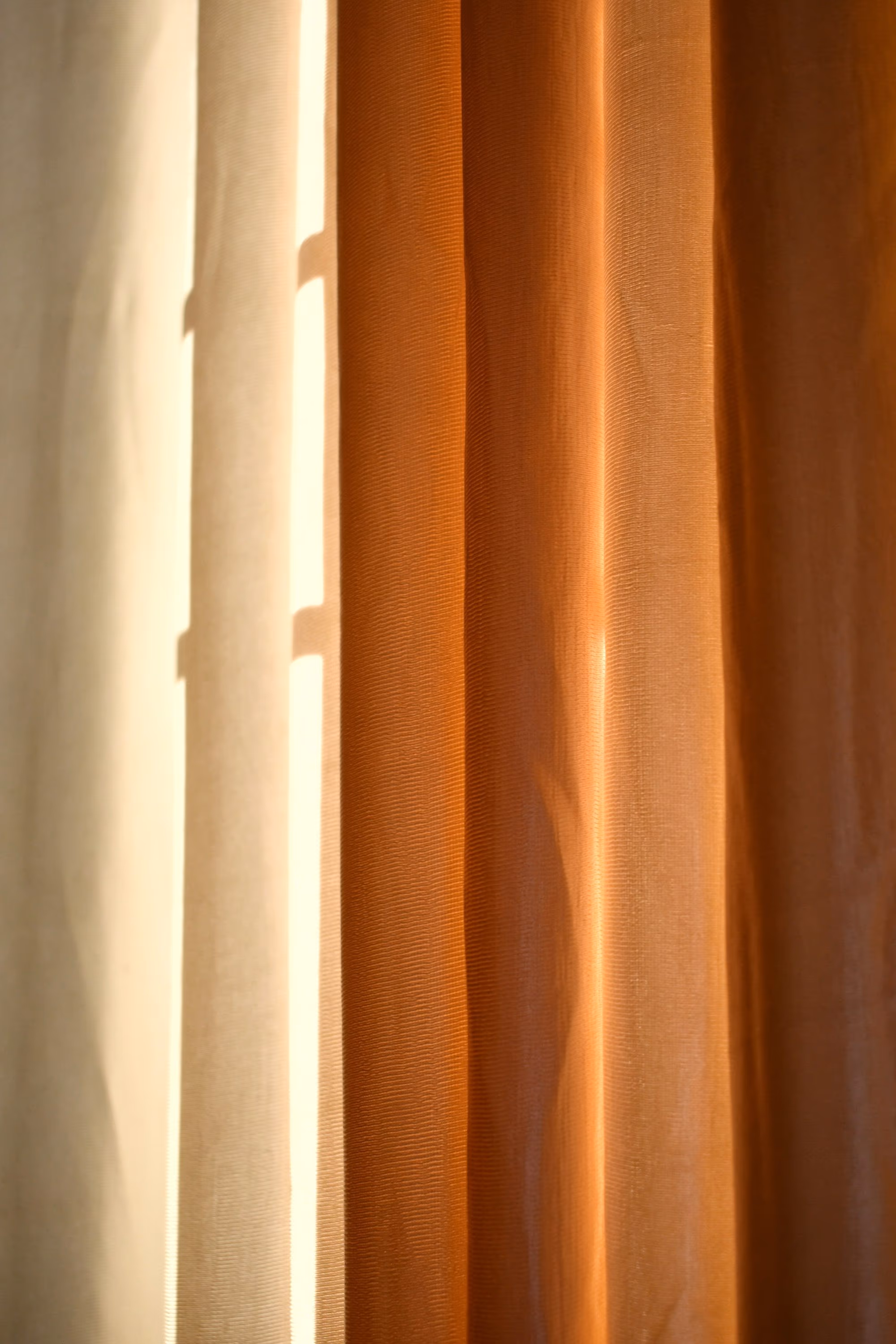 Rideau terracotta et voilage crème tirés, traversés par une lumière chaude