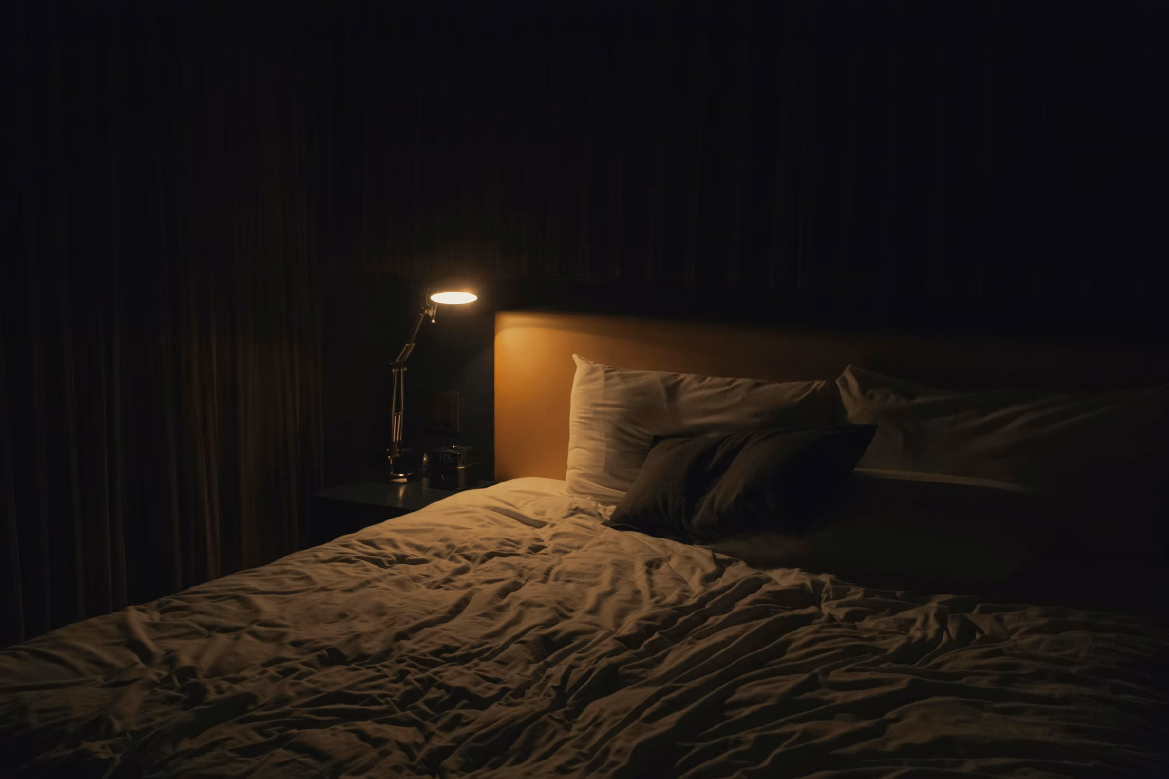 Chambre plongée dans la pénombre, éclairée par la lueur douce d’une lampe de chevet