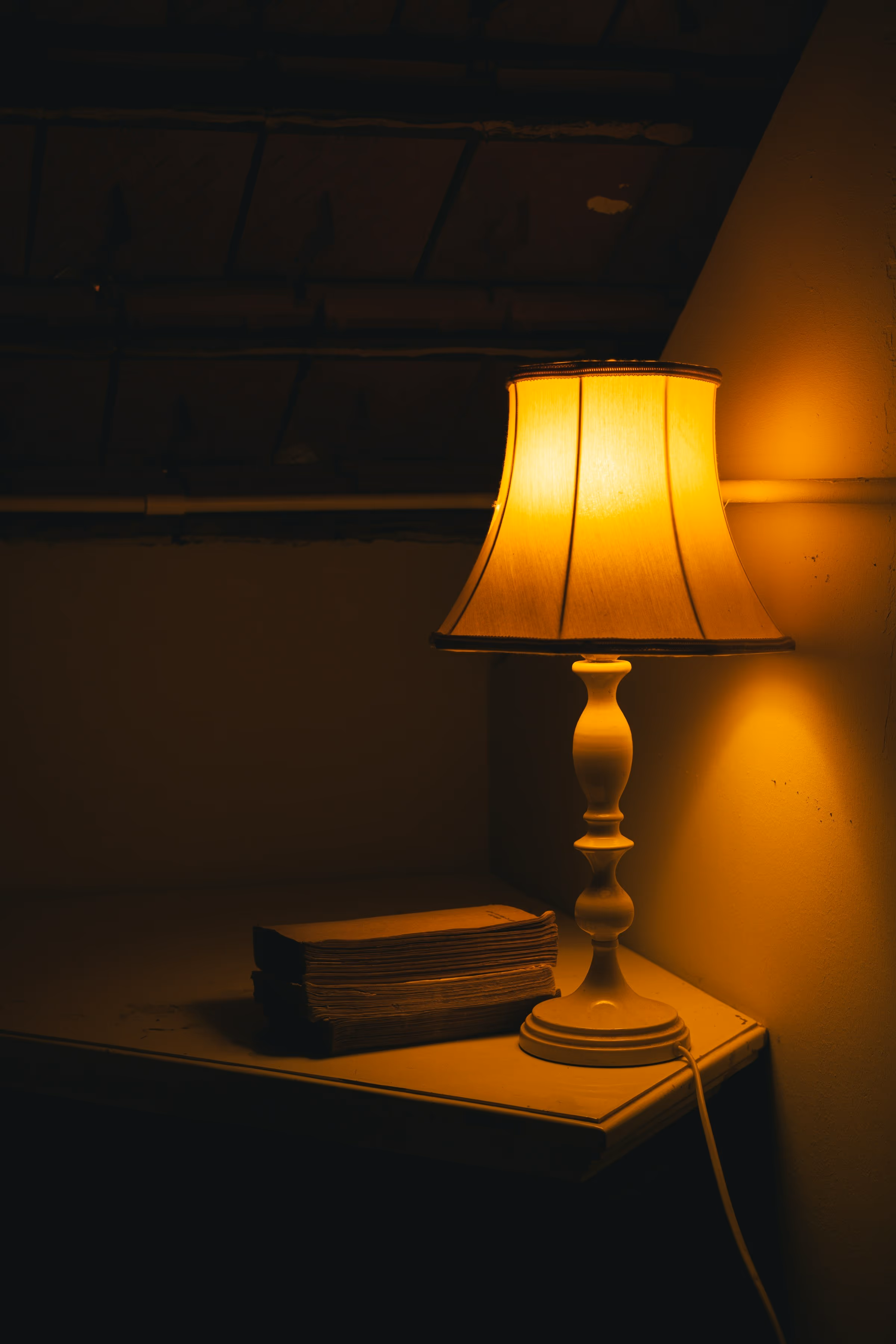 Lampe de chevet allumée dans la pénombre, à côté d’une petite pile de livres anciens sur une table de nuit