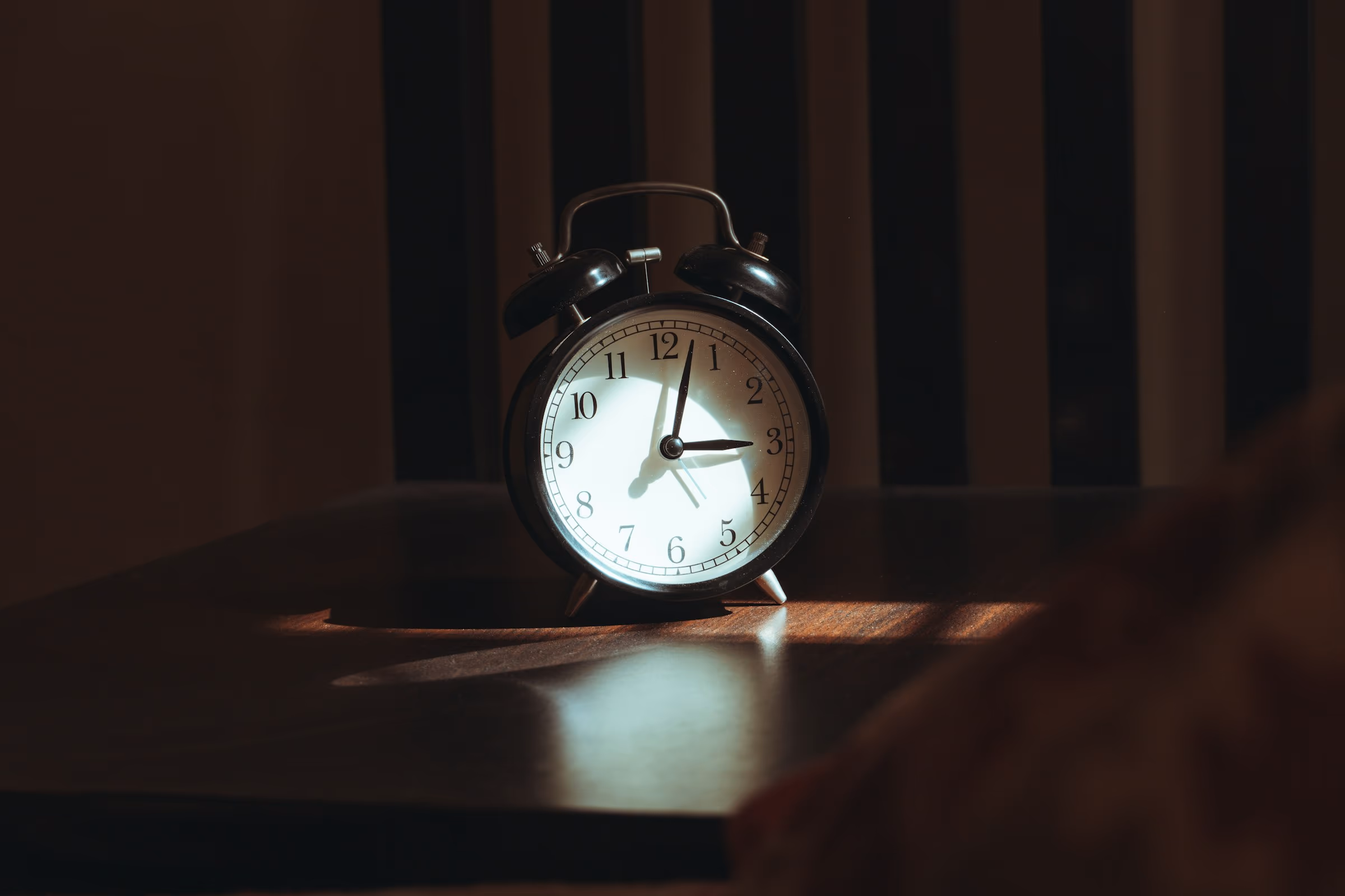 Réveil posé sur une table de nuit, aiguilles arrêtées sur les premières heures du matin