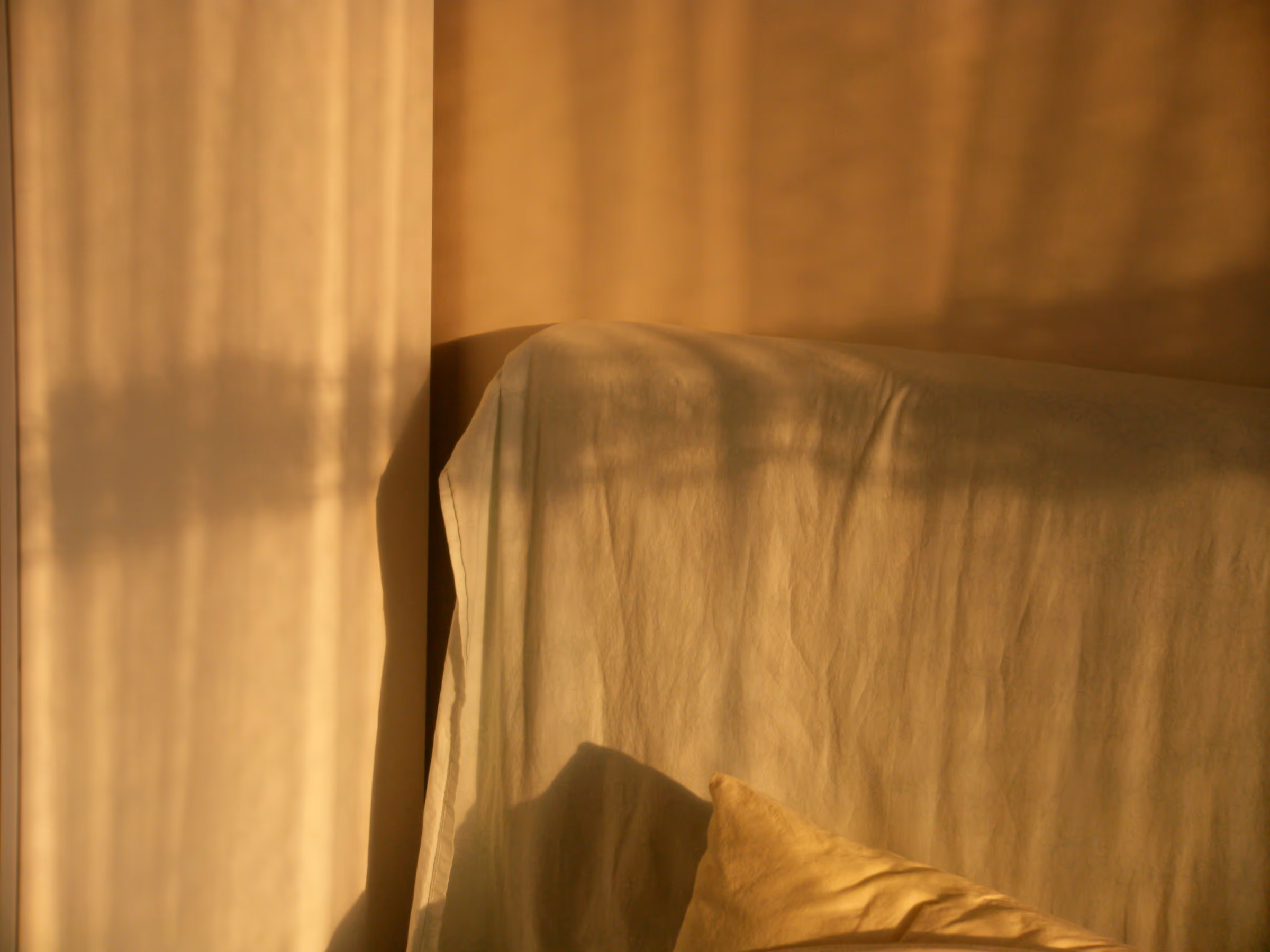 Drap de lin froissé recouvrant un lit, baigné d’une lumière dorée et d’ombres de rideau.