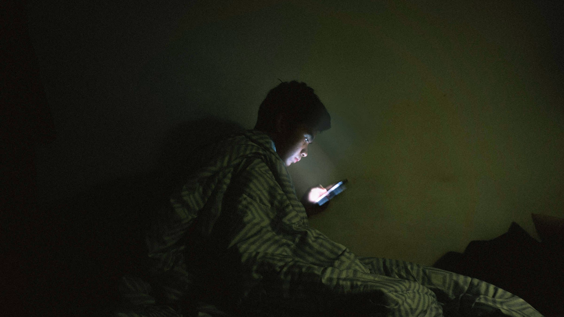 Téléphone éclairé posé sur un lit dans une chambre plongée dans la pénombre